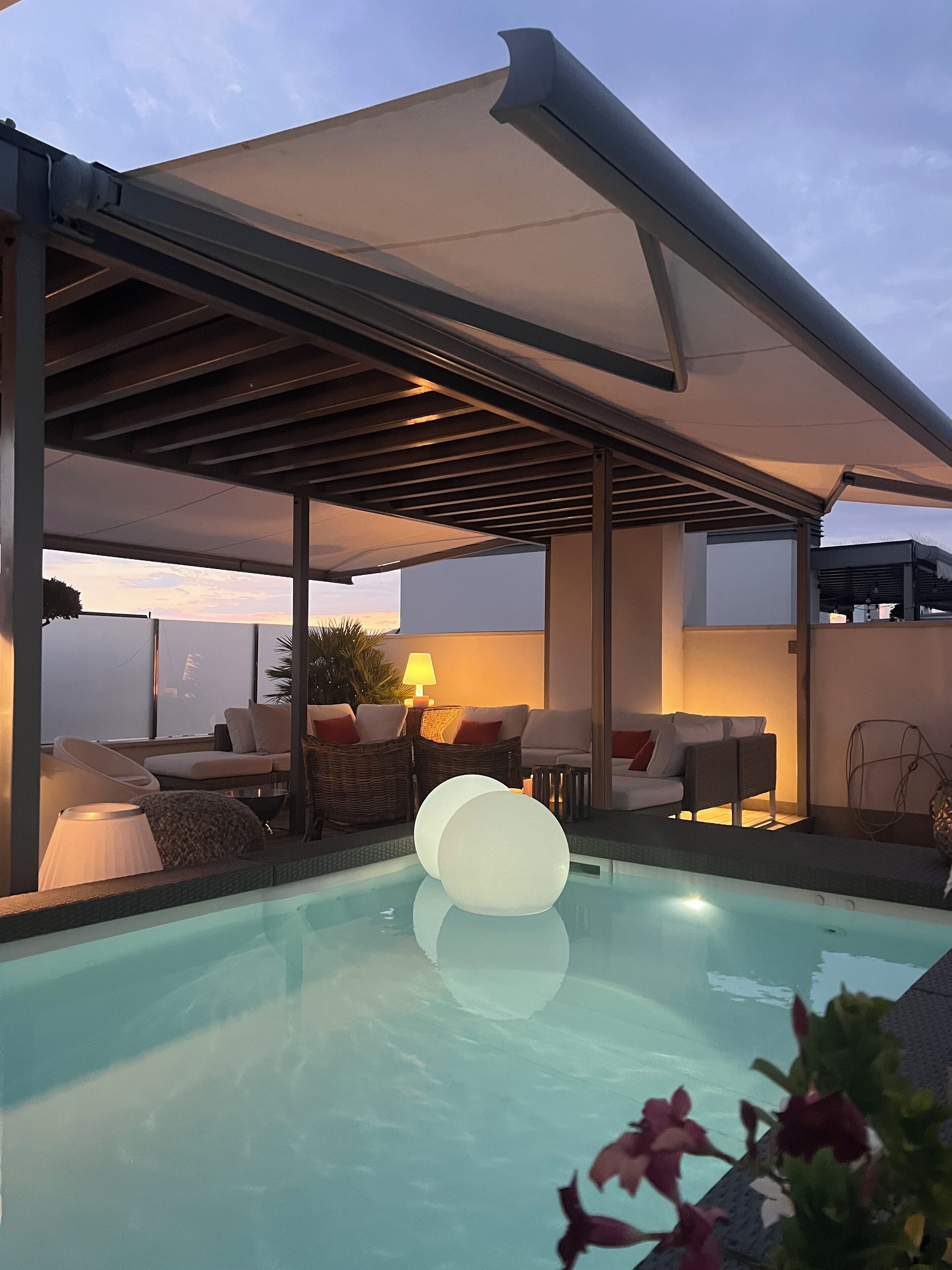 A modern outdoor pool area with a covered seating area, lounge chairs, and a poolside table.