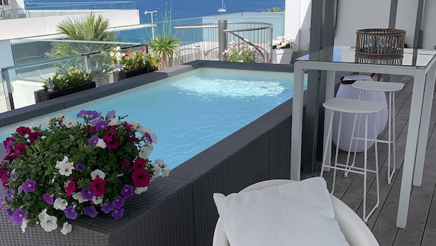 Zona de piscina en la azotea con cerramiento de vidrio, una silla de descanso blanca y una mesa con sillas.