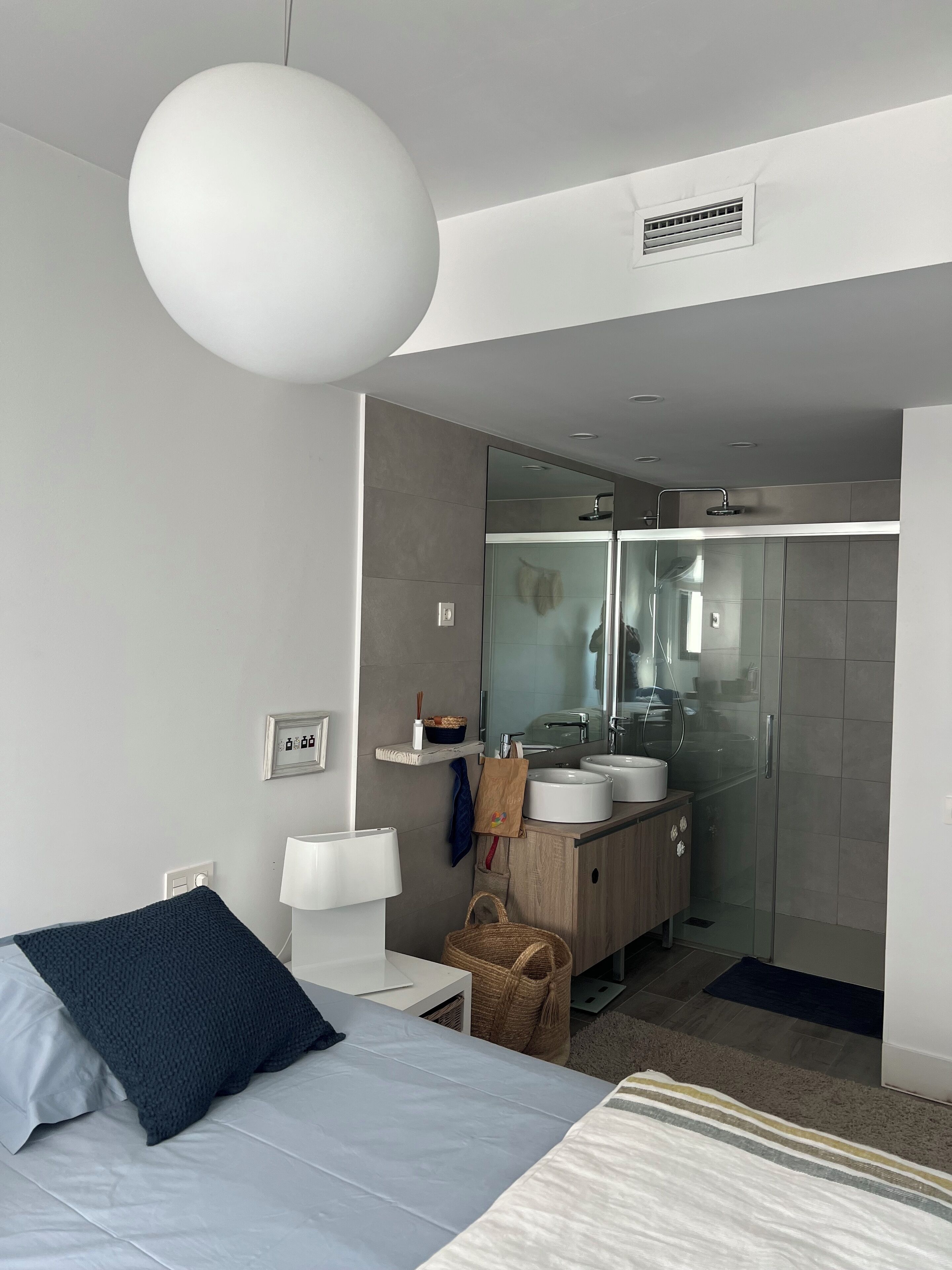 Ein modernes Hotelzimmer mit Bett, Nachttisch, Lampe und einem großen Spiegel.