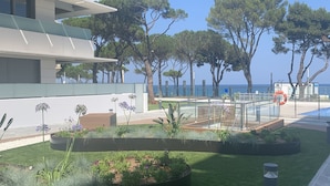 Un edificio moderno con techo plano y varios balcones, rodeado de jardines cuidados y vistas despejadas al mar.