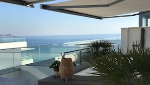 Un balcón con vista al mar, una silla de mimbre y una planta en maceta.