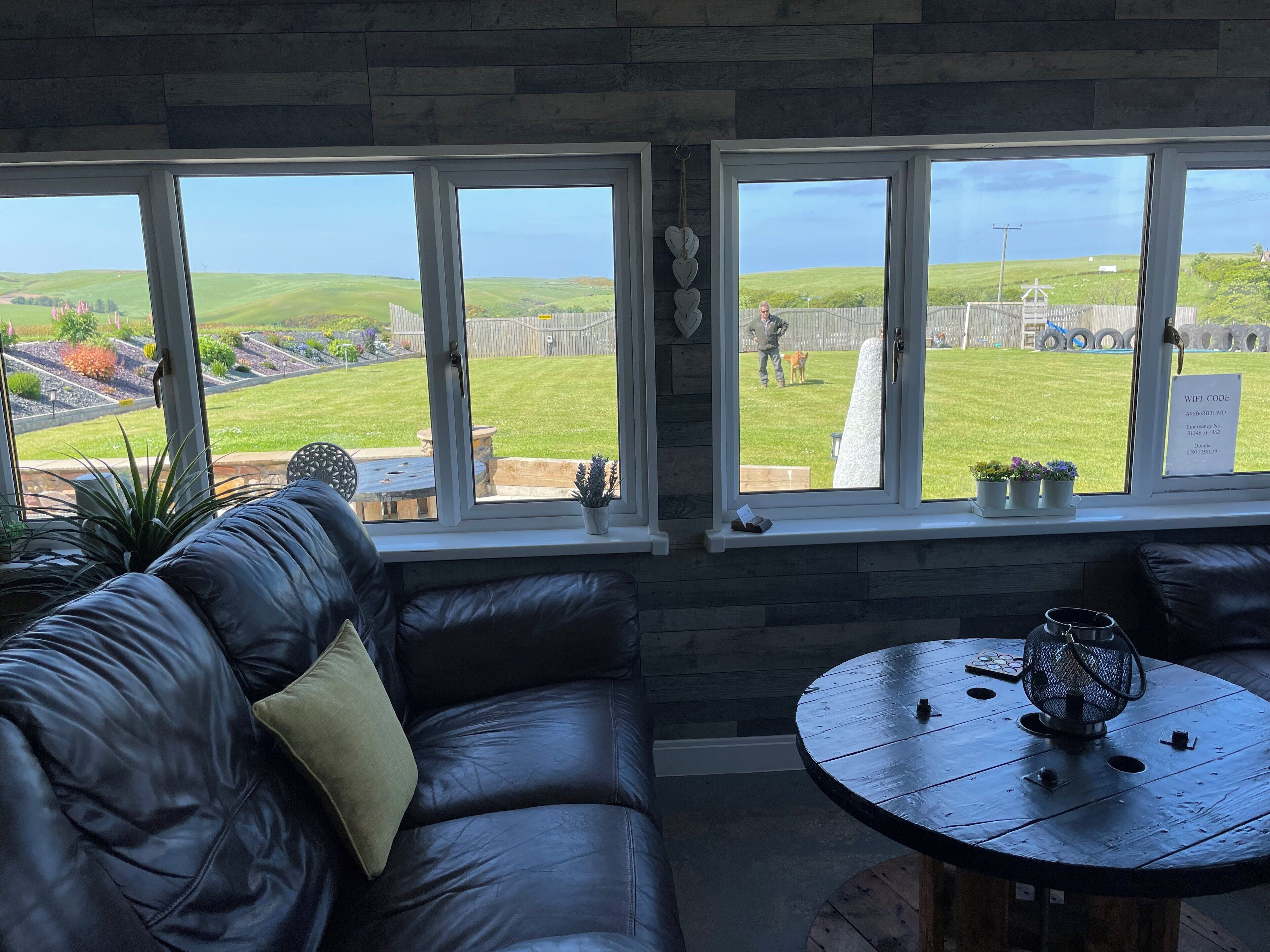 A room with a leather sofa, a round wooden table, and large windows overlooking a grassy yard.