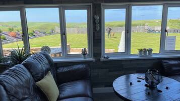 A room with a leather sofa, a round wooden table, and large windows overlooking a grassy yard.