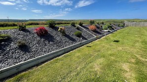 A landscaped garden with a gravel pathway, various shrubs, and a wooden fence. - Acdc Glamping, Campervan , Caravan and Tent Resort (Fraserburgh)