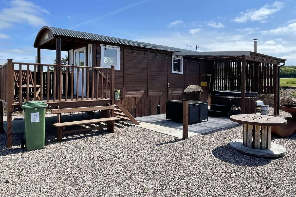 Una cabaña de madera con terraza, zona de barbacoa y suelo de grava.