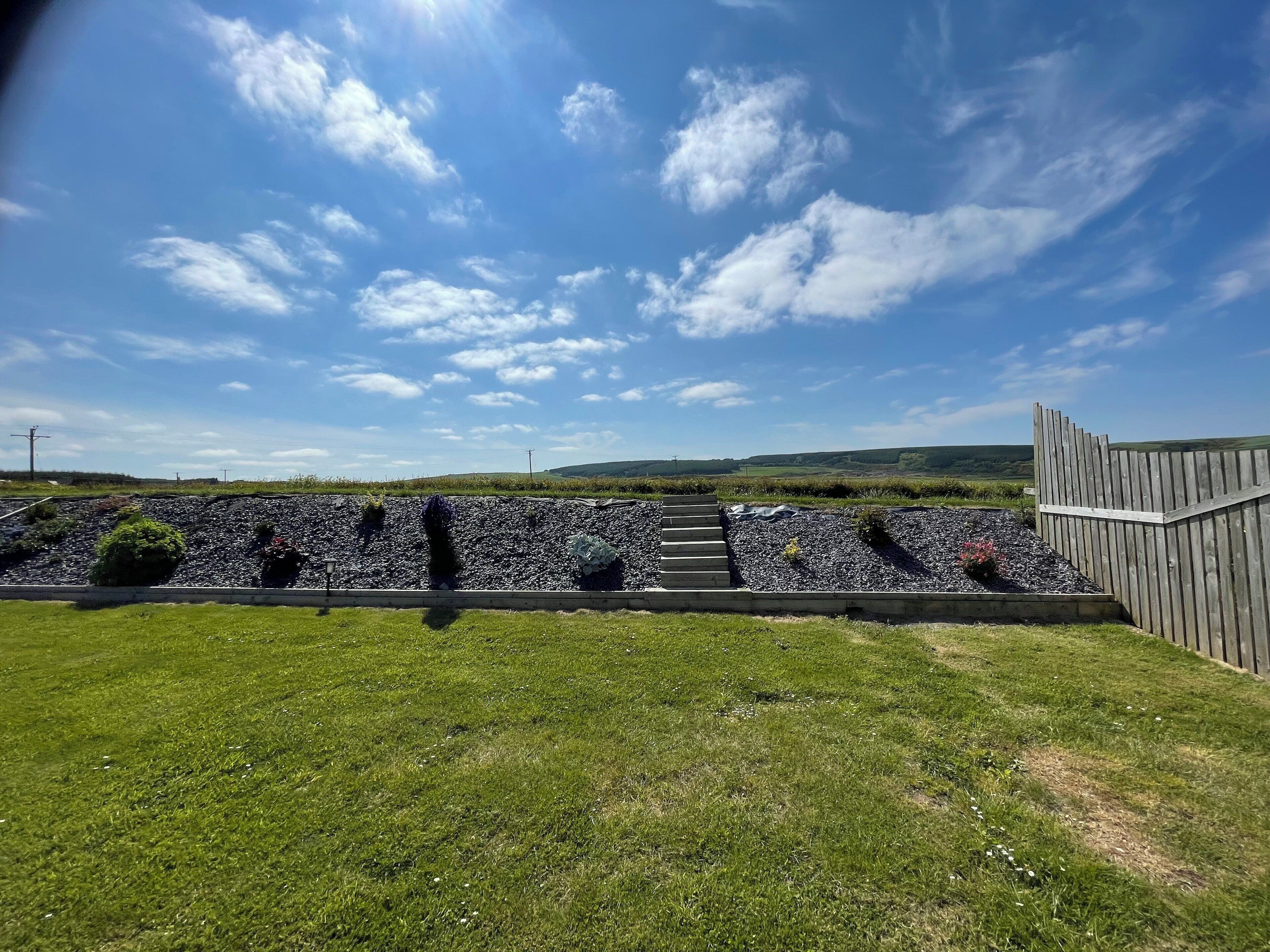 A grassy area with a stone wall and wooden fence.