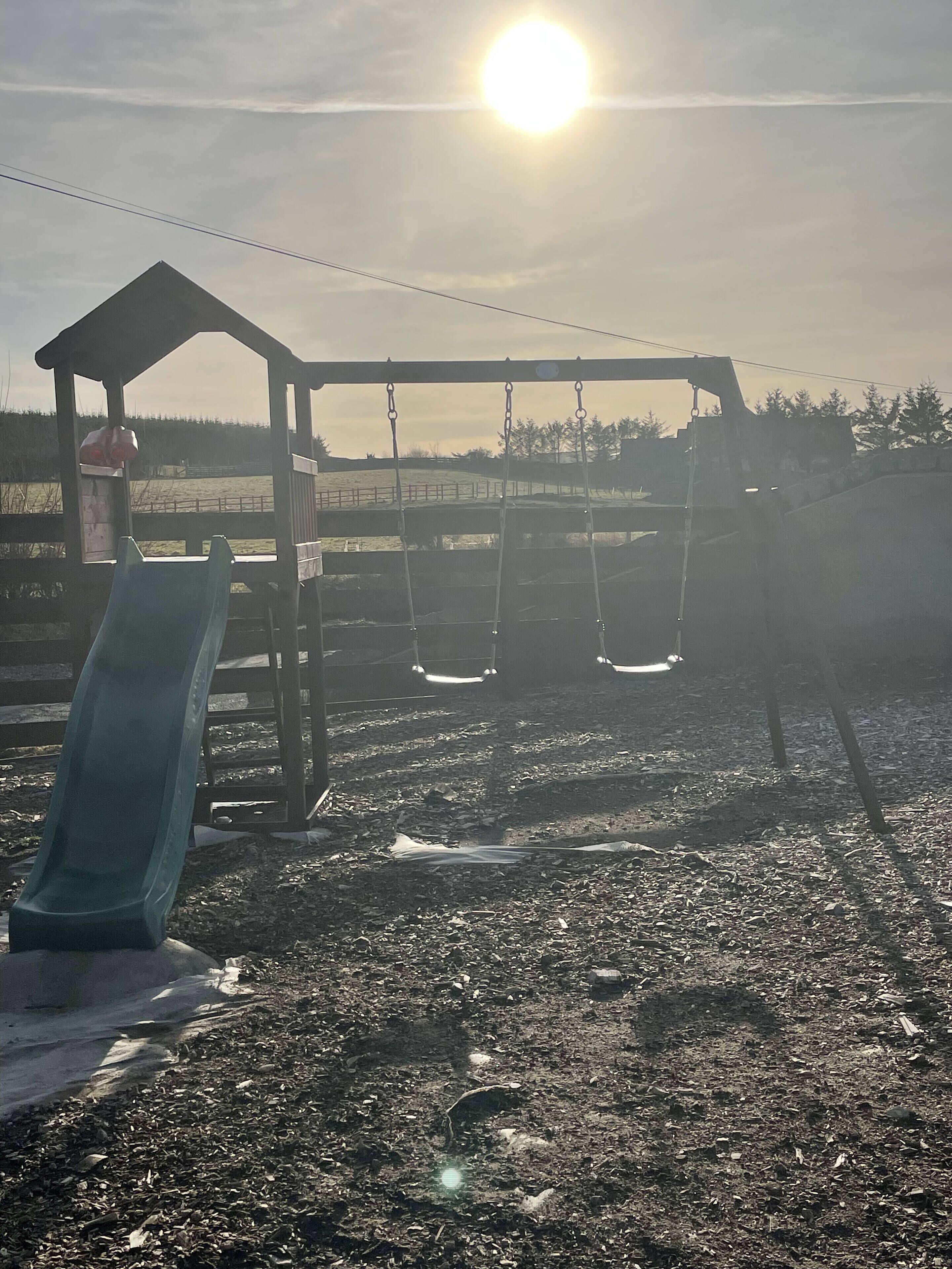 A playground with a slide and swings, set against a backdrop of trees and a clear sky.