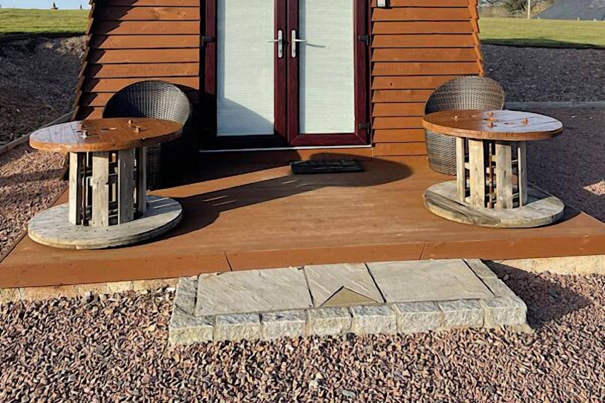 Una cabaña de madera con un letrero que dice "CABIN" y dos mesas redondas con sillas al frente.