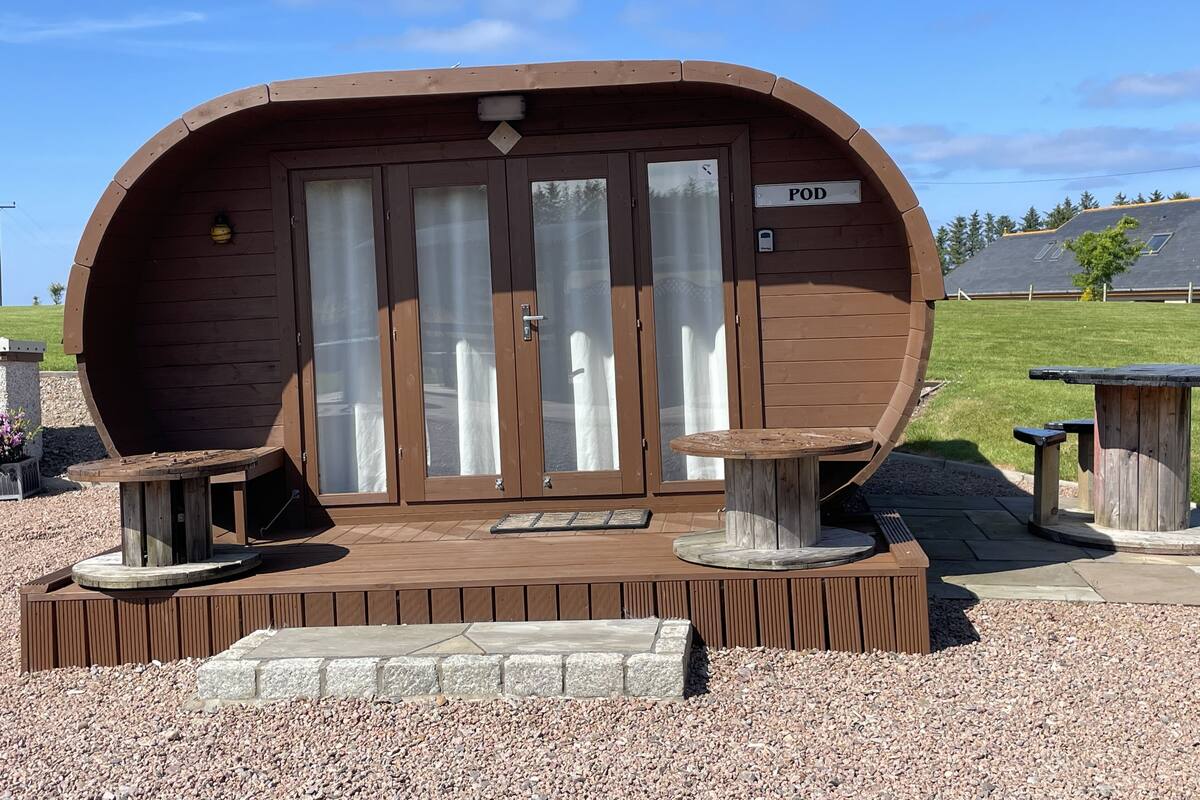 Una estructura tipo pod de madera con un letrero que dice "POD", una mesita y un banco.