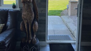 A room with a large wooden wall, a black leather couch, and a dog statue on a round black cushion. - Acdc Glamping, Campervan , Caravan and Tent Resort (Fraserburgh)