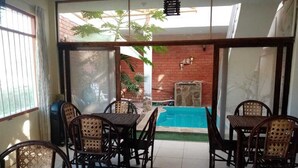 Un patio con piscina, rodeado de mobiliario de mimbre y un muro de ladrillo.