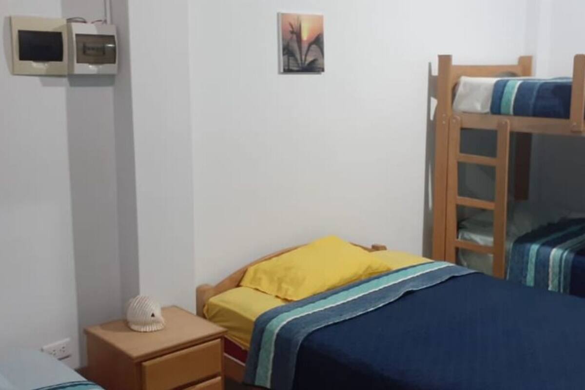A bunk bed room with a wooden ladder, a bedside table, a yellow pillow, and a small white lamp.