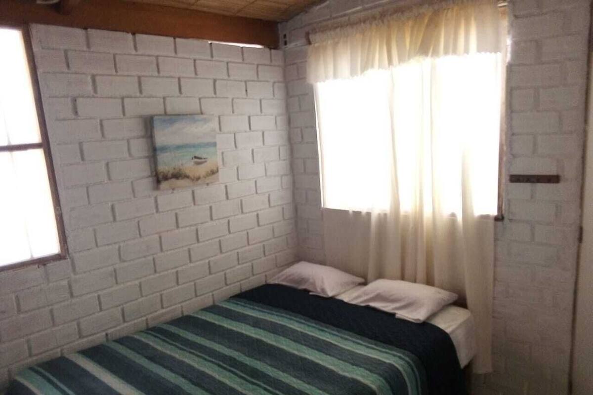 A single-bed room with a brick-patterned wall, a painting, and a window with curtains.