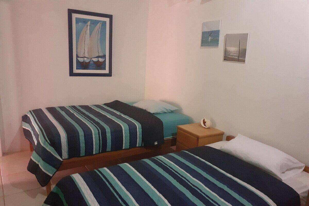 A room with two beds, each with striped bedding, a small bedside table, and a framed picture on the wall.