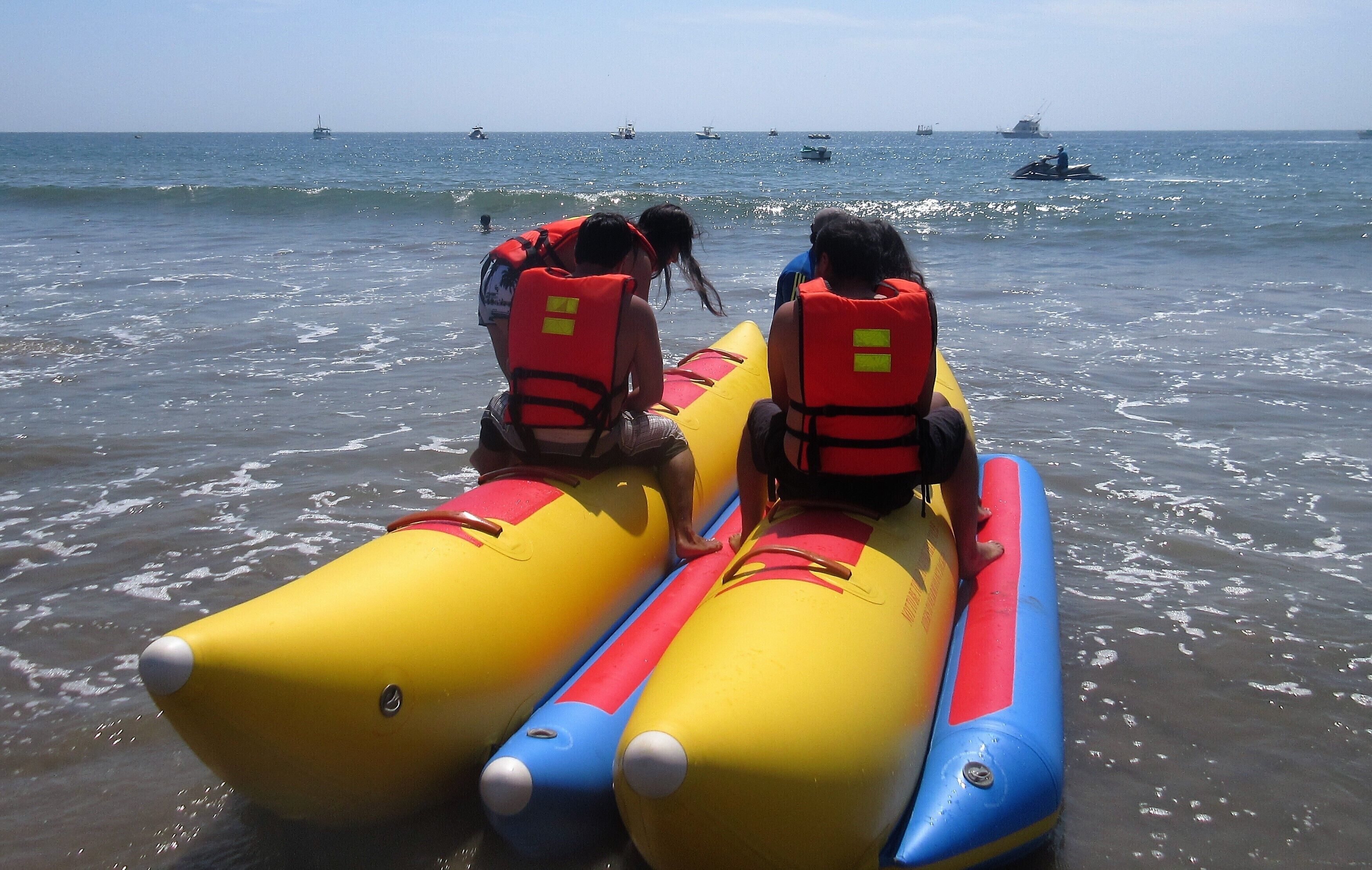 Tres personas en balsas inflables en la playa, con embarcaciones al fondo.