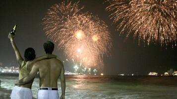 Dos personas junto al agua observando fuegos artificiales.