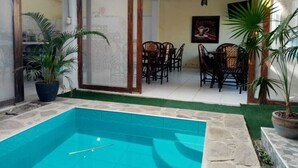 Una piscina interior con paredes de azulejos, rodeada de plantas en macetas y muebles de madera.