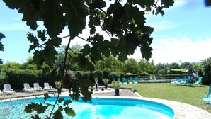 En swimmingpool med en kant av sten, omgiven av solstolar och en gräsyta.