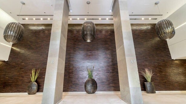 Eine moderne Lobby mit dunklen Holzvertäfelungen, drei großen, kugelförmigen Leuchten und zwei Zimmerpflanzen.