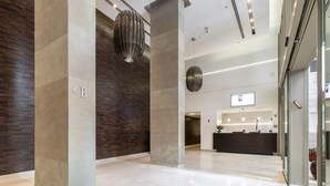 Eine geräumige Lobby mit einer Rezeption, modernen Leuchten und einer großen Säule mit einem Buchstaben.