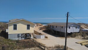 Une maison de plage avec une allée sablonne menant à l’océan, un petit porche et un abri de jardin.
