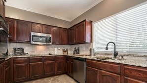 A kitchen with dark wooden cabinets, a stainless steel microwave, and a dishwasher. - 4 Bedroom With Landscaped Private Pool & Outdoor Pool Table ~MONTHLY DISCOUNT~ (McKinney)
