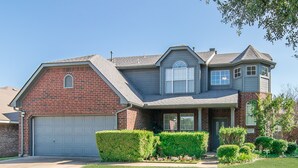 A two-story house with a garage, a front porch, and a well-maintained lawn. - 4 Bedroom With Landscaped Private Pool & Outdoor Pool Table ~MONTHLY DISCOUNT~ (McKinney)