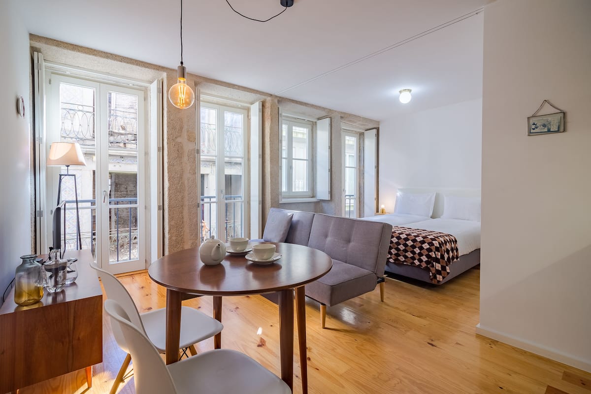 Una habitación moderna con sofá, una mesa de comedor con sillas, cama y ventanas amplias.
