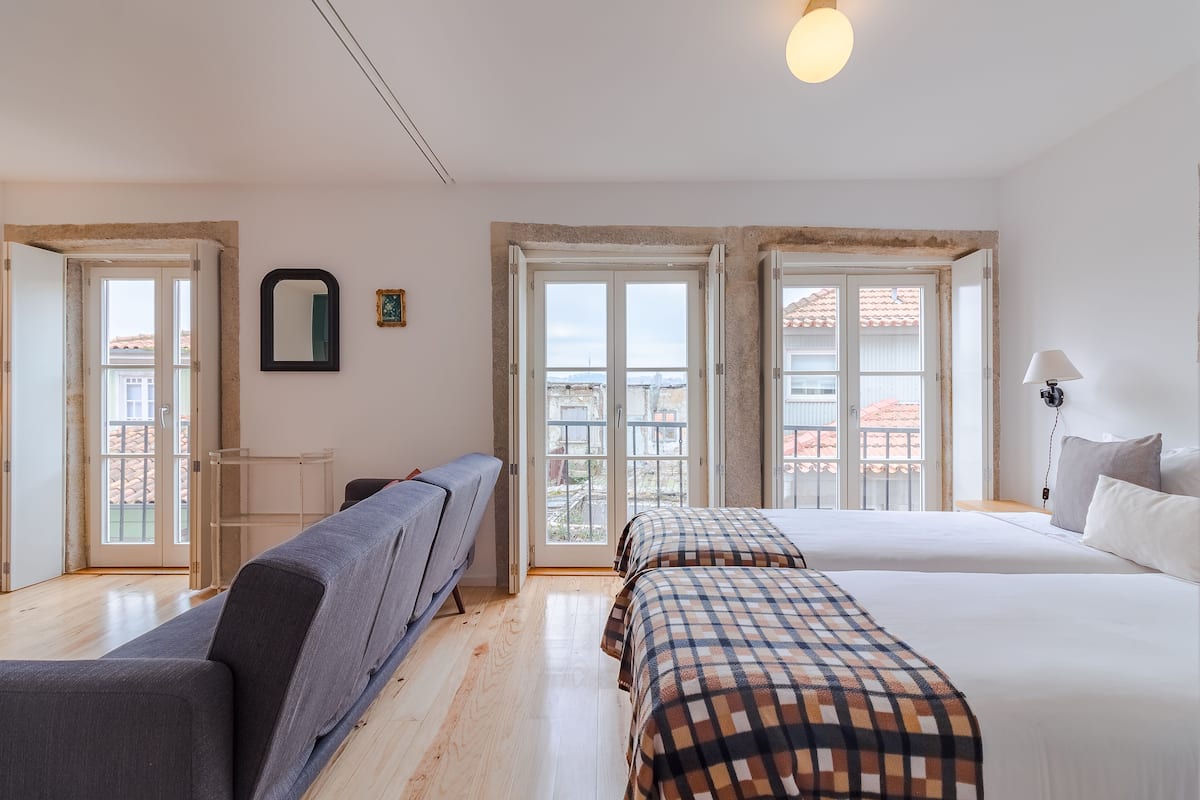 Un dormitorio con dos camas, un sofá, un espejo y una ventana con vistas a edificios.