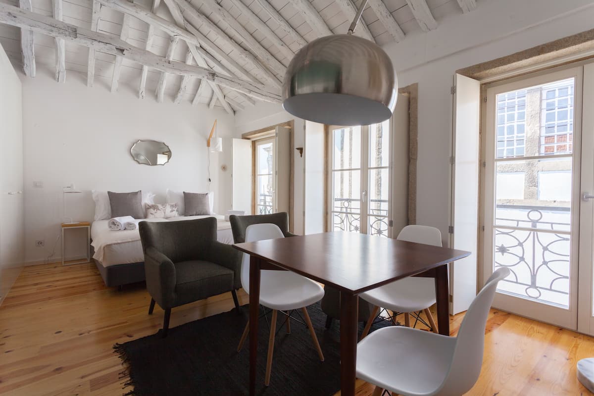 Un salón moderno con suelo de madera, una mesa de comedor con sillas, un sofá y un amplio ventanal con balcón.