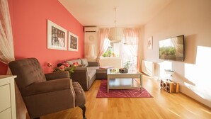 Ein Wohnzimmer mit Sofa, Sessel, Couchtisch und einem an der Wand befestigten Fernseher.