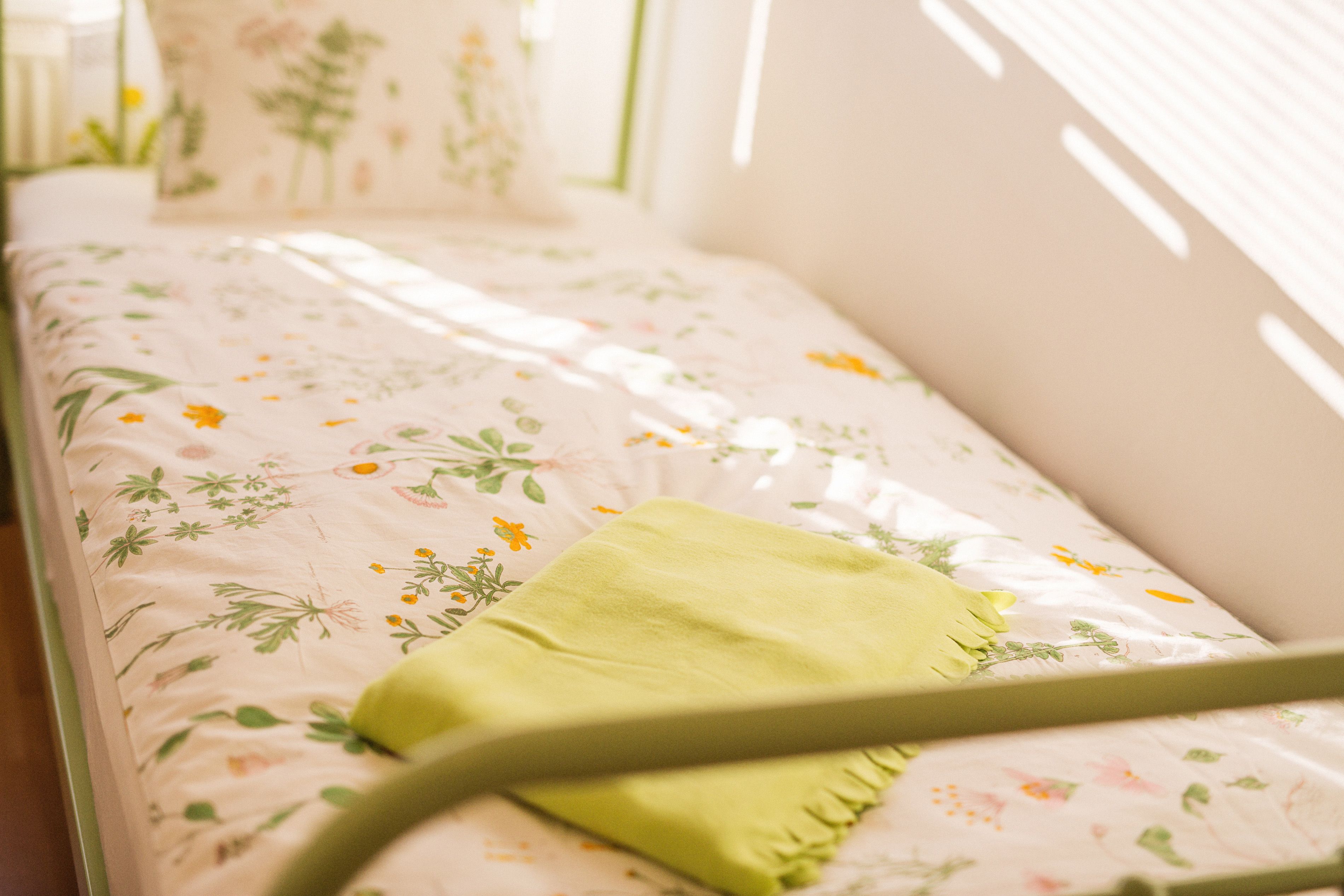 A bed with floral bedding and a green pillow.