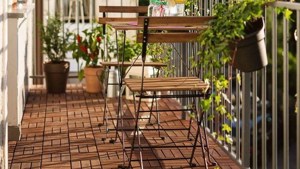 Ein Balkon mit Holztisch und -stühlen, Blumentöpfen und Blick auf die Berge.