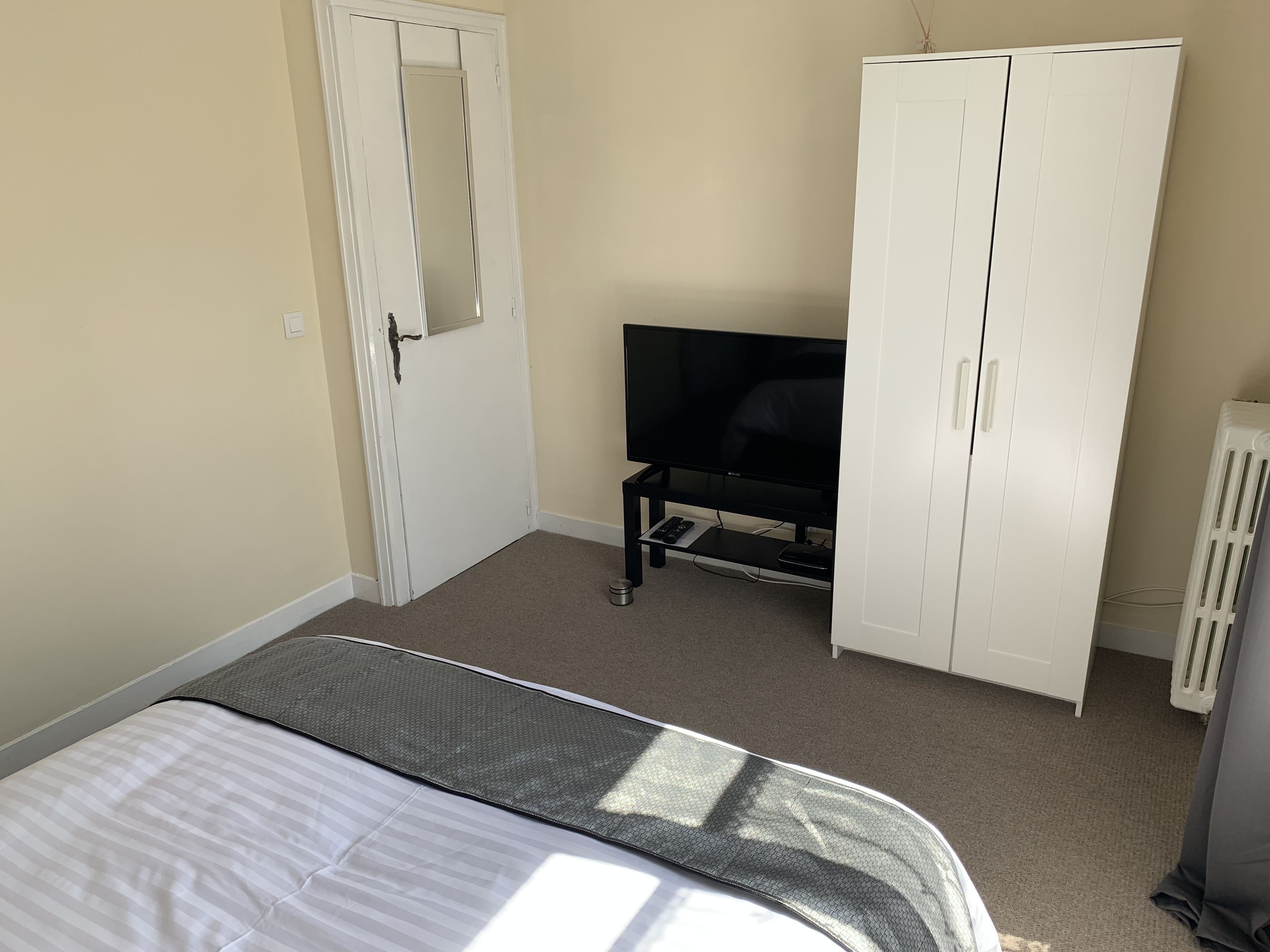 A bedroom with a bed, a TV, a wardrobe, and a radiator.