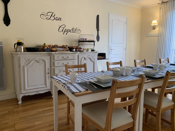 A dining area with a table set for four, wooden chairs, a white cabinet with drawers, and a wall-mounted knife.