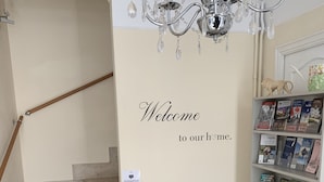 A staircase with a 'Welcome to our home' sign, a radiator, and a bookshelf with books. - No 6 Bed & Breakfast (Landivy)