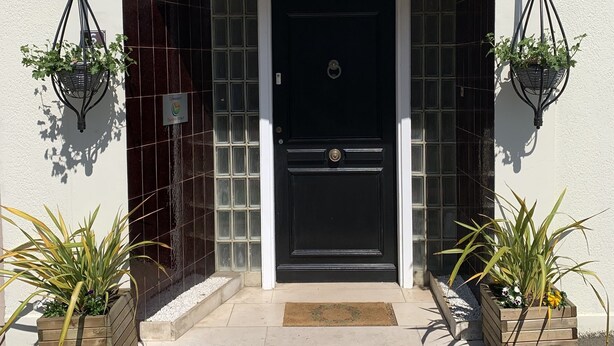 A building entrance with a black door, a sign above reading "N°6 B&B", and two hanging planters with plants on either side. - No 6 Bed & Breakfast (Landivy)