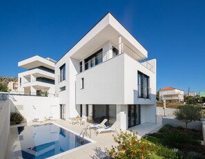 Una casa moderna de dos pisos con piscina, mobiliario exterior y jardín.
