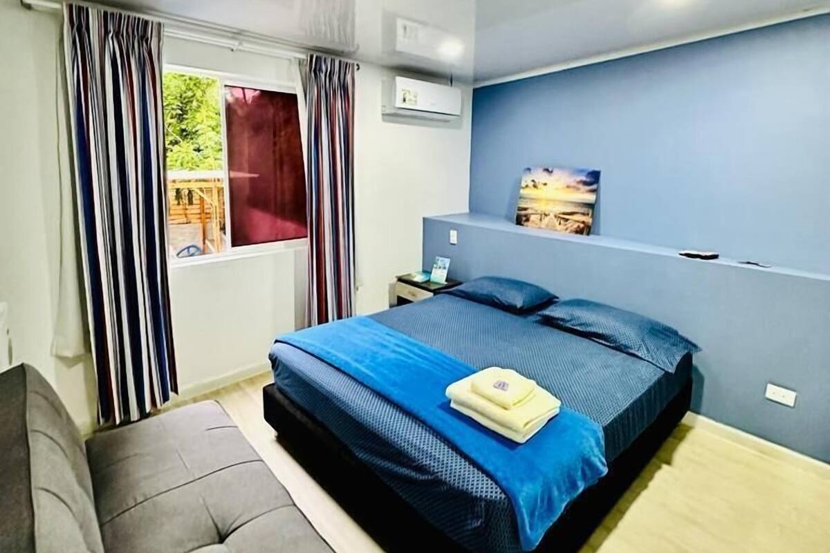 A bedroom with a bed, a nightstand, a window with curtains, and a painting on the wall.