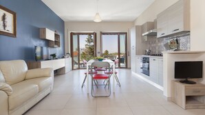 A modern kitchen with a dining area, a sofa, and a TV.