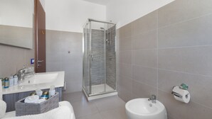A modern bathroom with a glass-enclosed shower, a sink with a mirror, and a bidet.
