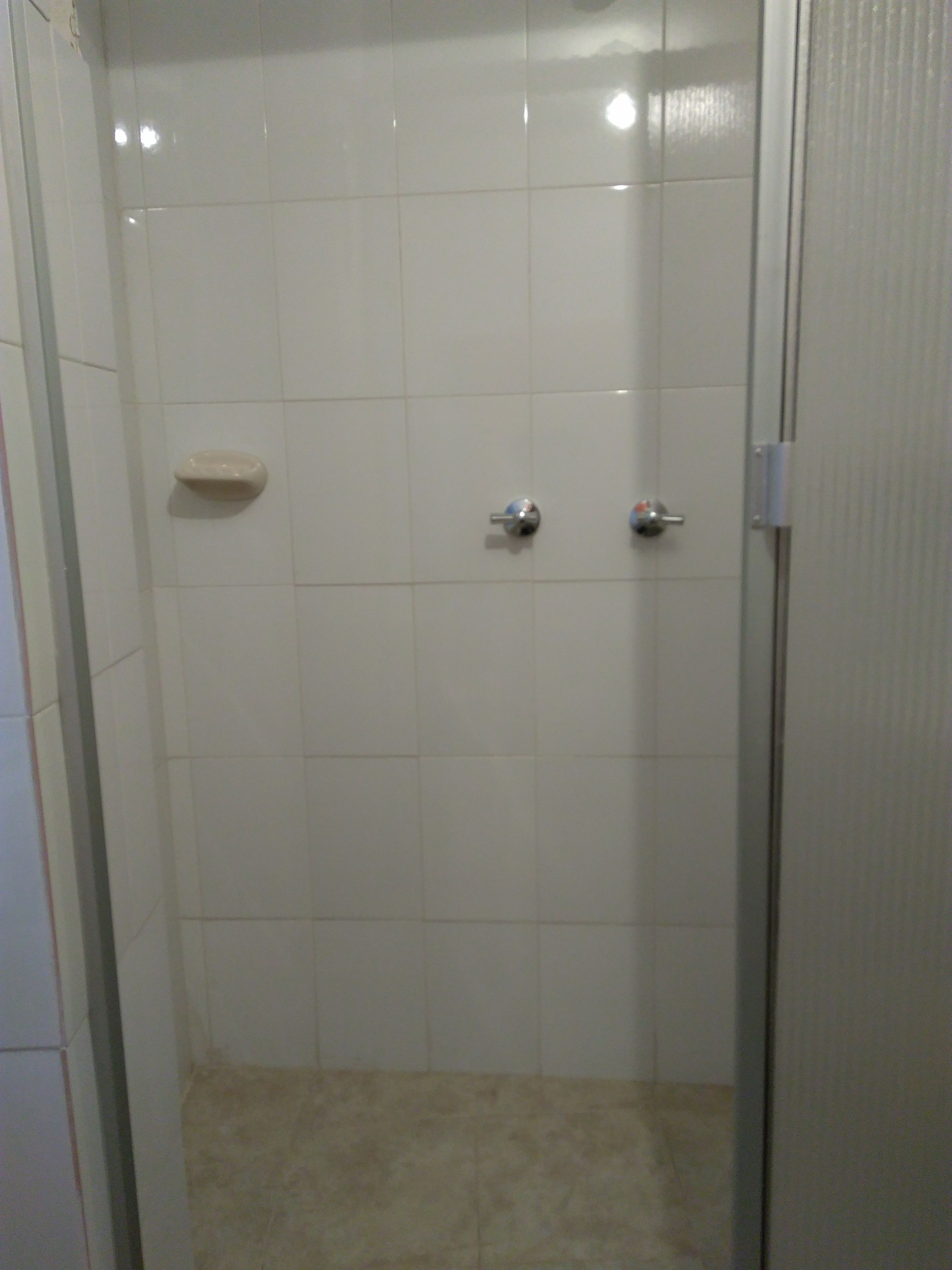 Un espacio de ducha pequeño y cerrado, con azulejos blancos y suelo color beige.