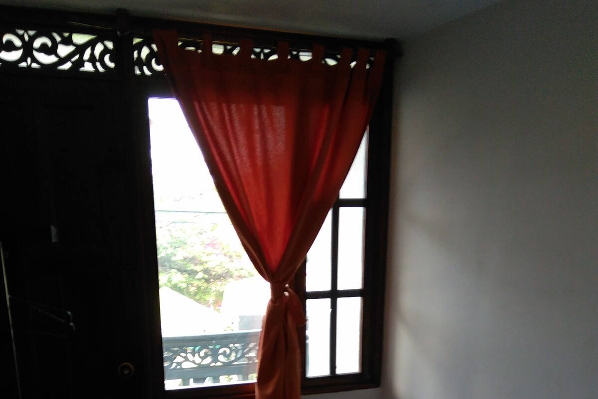 Ein Schlafzimmer mit einem Bett, einem Fenster mit Vorhängen, einer Tür und einem Fliesenboden.