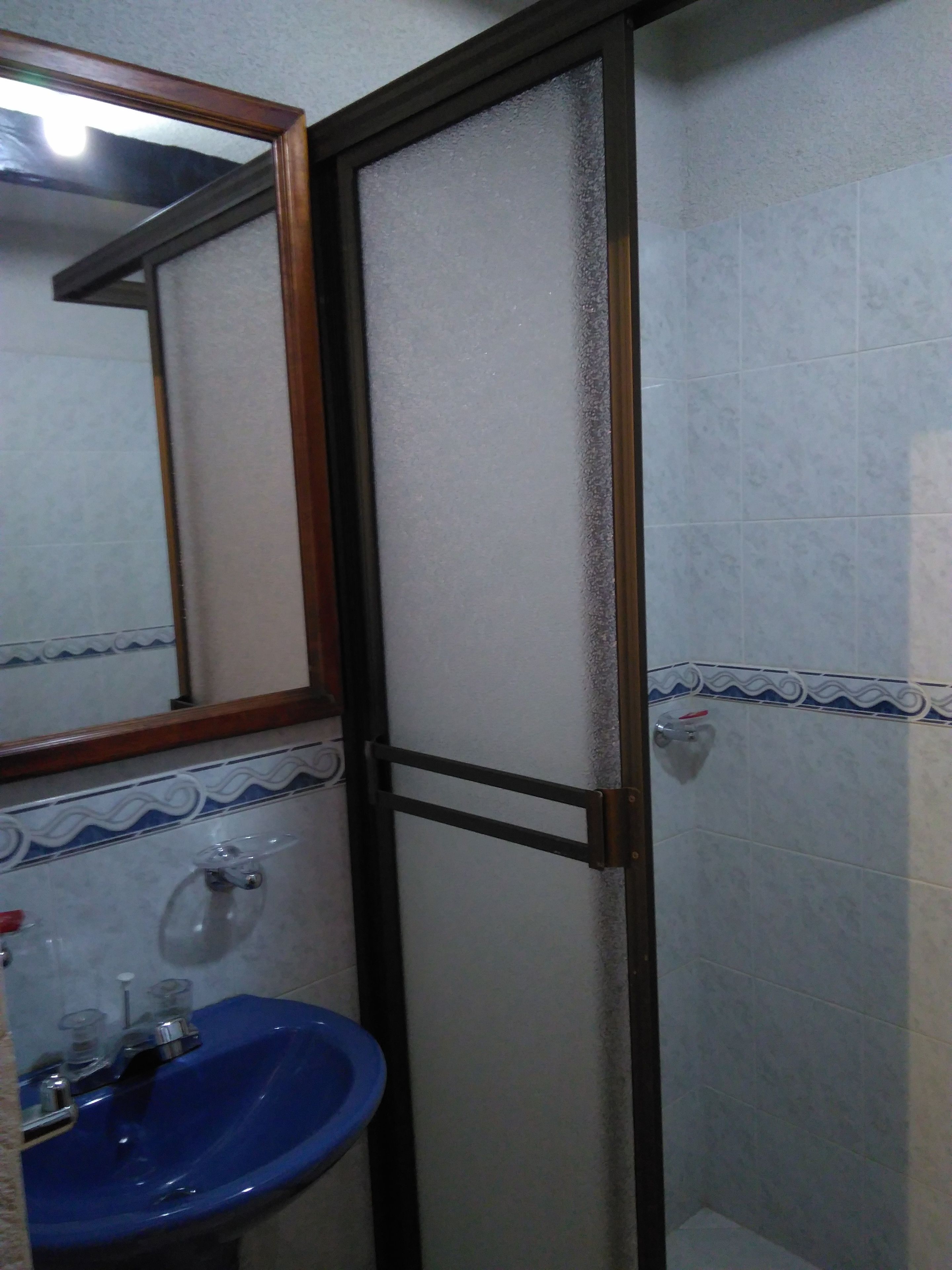 Een badkamer met een blauwe wastafel, een spiegel en betegelde wanden.
