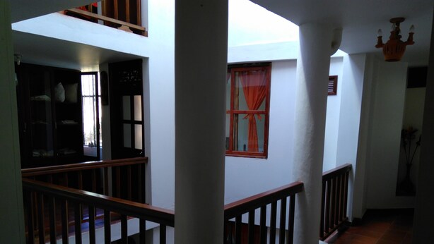 A multi-level interior with a wooden railing, a window with orange curtains, and a tiled floor. - Hotel Rural Posada de los Santos (Ráquira)
