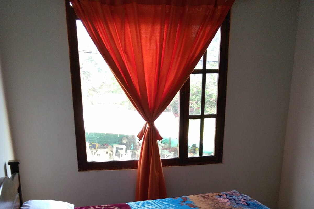 Ein Bett mit farbenfroher Bettdecke, ein Fenster mit Vorhang und Blick nach draußen.