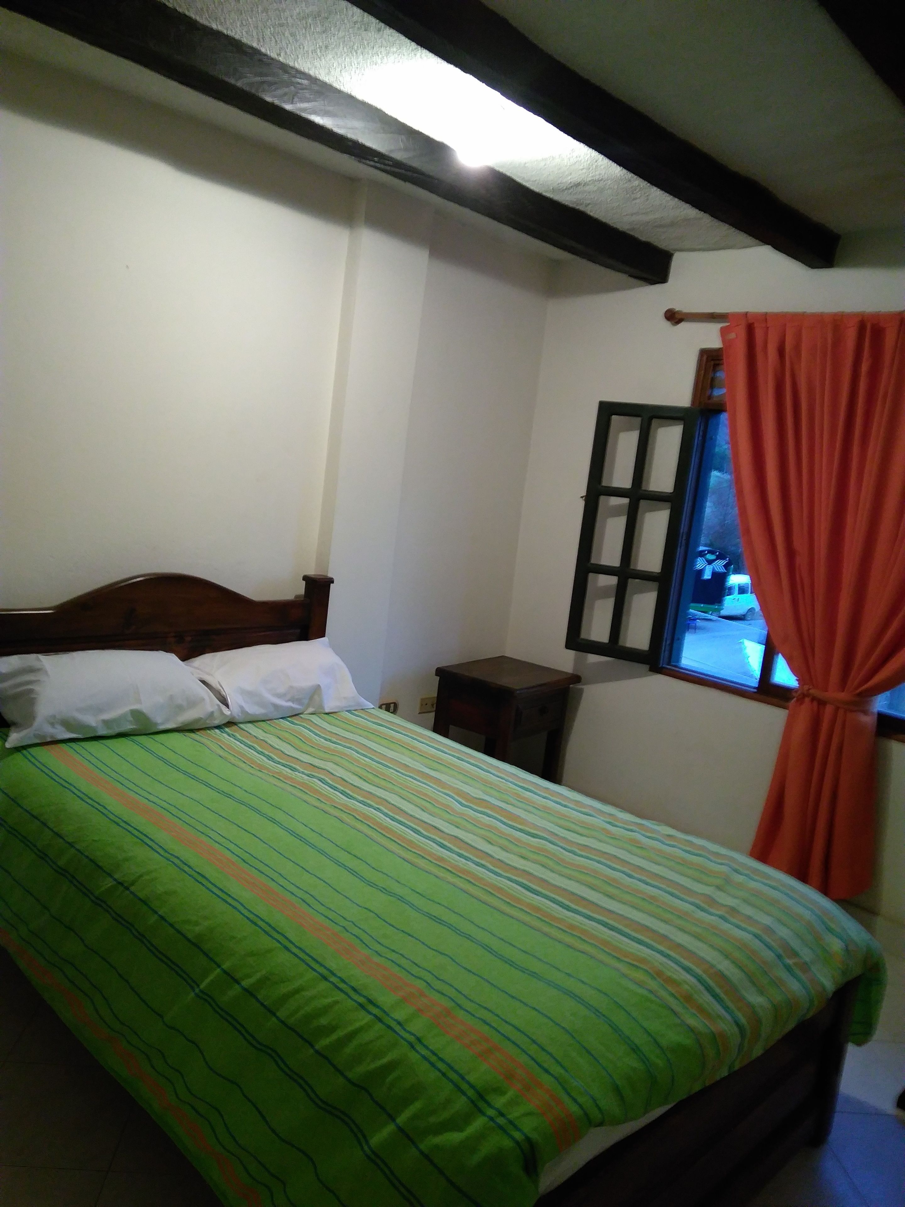 Un dormitorio con cama, una mesita de noche, una ventana con cortinas y una viga de techo de madera.
