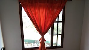A bedroom with a bed, a window with curtains, and a view of the outside. - Hotel Rural Posada de los Santos (Ráquira)