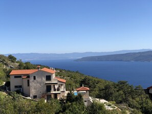 Una propiedad costera con un edificio de piedra, una piscina y vistas al mar y montañas distantes.