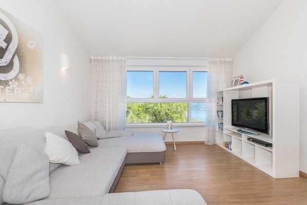 A modern living room with a large window, a sofa, a TV, and a bookshelf.